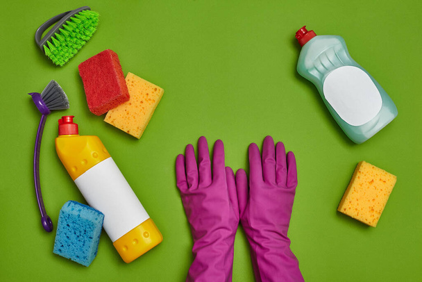 Detergentes de alta calidad y accesorios de limpieza, como: esponjas multicolores, desinfectante de etiquetas vacío y limpiador para platos, cepillos y guantes de goma violeta sobre fondo verde. Limpieza - Foto, imagen