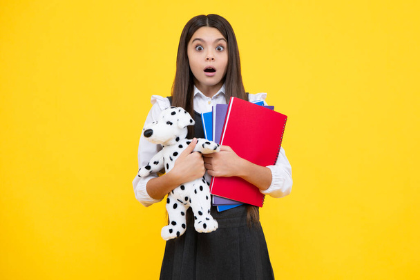 Αστείο κορίτσι του σχολείου με παιχνίδι απομονωμένο σε κίτρινο φόντο. Ευτυχισμένη παιδική ηλικία και εκπαίδευση παιδιών. Έκπληκτος πρόσωπο, έκπληξη συναισθήματα της έφηβης κορίτσι - Φωτογραφία, εικόνα