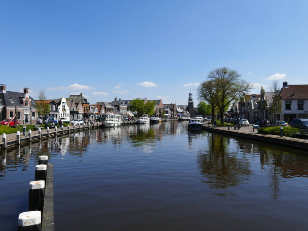 Szeroki kanał biegnie przez (holenderski) Lemmer (fryzyjski) De Lemmer (miasto portowe na Ijsselmeer, bardzo duże jezioro), Friesland, Holandia, jest popularny zarówno wśród żeglarzy rekreacyjnych i turystów, z licznymi restauracjami i sklepami po obu stronach - Zdjęcie, obraz