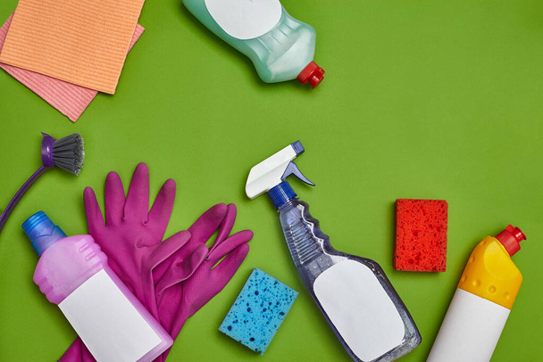 Detergentes de alta calidad y accesorios de limpieza, como: esponjas multicolores, desinfectante de etiquetas vacío, spray y limpiador para platos, cepillo, guantes de goma violeta y paños de cocina rosa sobre un verde - Foto, imagen