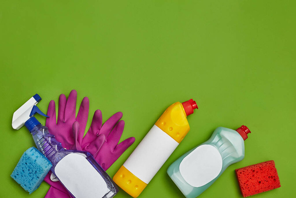 Detergentes de alta calidad y accesorios de limpieza, como: esponjas multicolores, aerosol de etiquetas vacío y limpiador para platos, guantes de goma violeta sobre fondo verde. Servicio de limpieza, pequeña empresa - Foto, imagen