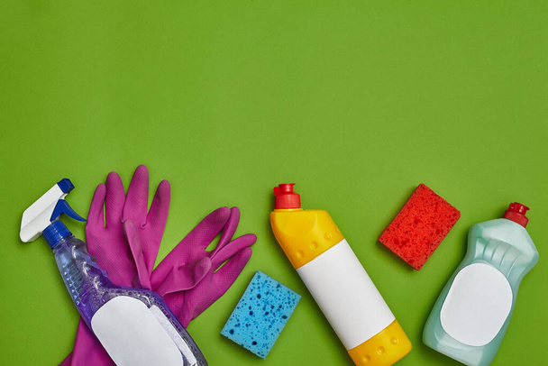 Detergentes originales y accesorios de limpieza, como: esponjas multicolores, aerosol de etiquetas vacío y limpiador para platos, guantes de goma violeta sobre fondo verde. Servicio de limpieza, pequeña empresa - Foto, imagen