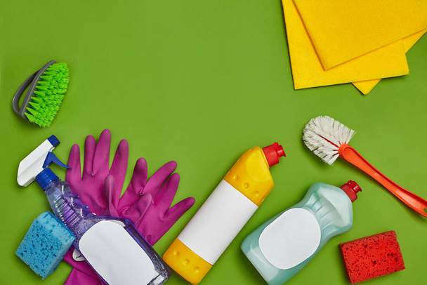 Originele wasmiddelen en reinigingsaccessoires, zoals: kleurrijke sponzen, spray en reinigingsmiddel voor gerechten met een leeg etiket, twee borstels, paarse rubberen handschoenen en vaatdoeken op een groene achtergrond - Foto, afbeelding