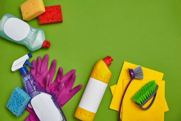 Professionele wasmiddelen en reinigingsaccessoires, zoals: kleurrijke sponzen, spray en reinigingsmiddel voor gerechten met een leeg etiket, twee borstels, paarse rubberen handschoenen en vaatdoeken op een groene achtergrond - Foto, afbeelding