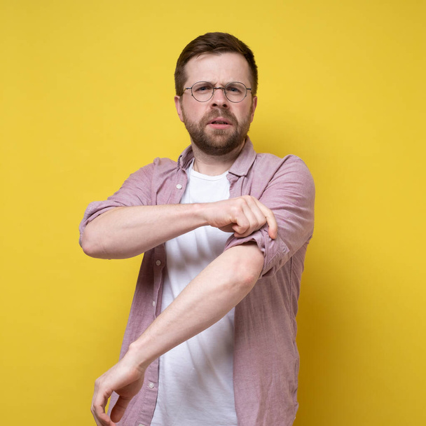 Calm Caucasian man in glasses, rolls up his shirt sleeves and peers into the distance. Isolated, yellow background. - Fotoğraf, Görsel