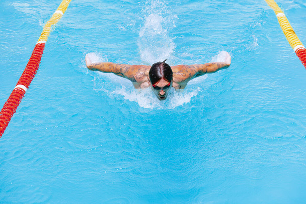 Дыши. Техника плавания бабочек. Молодой мускулистый человек, профессиональный пловец в очках, тренирующийся в общественном бассейне, на открытом воздухе. Спорт, сила, энергия, стиль, хобби-концепция. Небесно-голубая вода - Фото, изображение