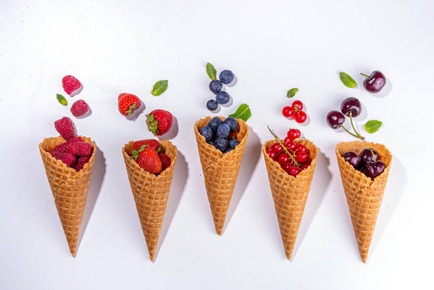 Waffle cones with fresh summer berries. Berry gelato, ice cream concept with raspberry, strawberry,  blueberry, cherry, currant in waffle cones on a white background - Photo, Image