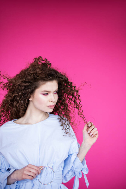 Fashion model girl with curly wavy shiny healthy hair on pink background Hair care bright makeup - Fotó, kép