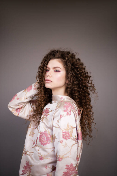 Fashion model girl with curly wavy shiny healthy hair on grey background. Hair care, bright makeup - Φωτογραφία, εικόνα