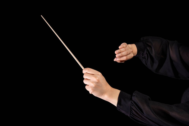 Conductora femenina dirigiendo una sinfonía con su bastón sobre un fondo negro - Foto, Imagen