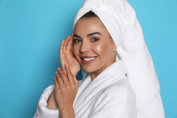 Beautiful young woman wearing bathrobe and towel on head against light blue background - Foto, Imagen