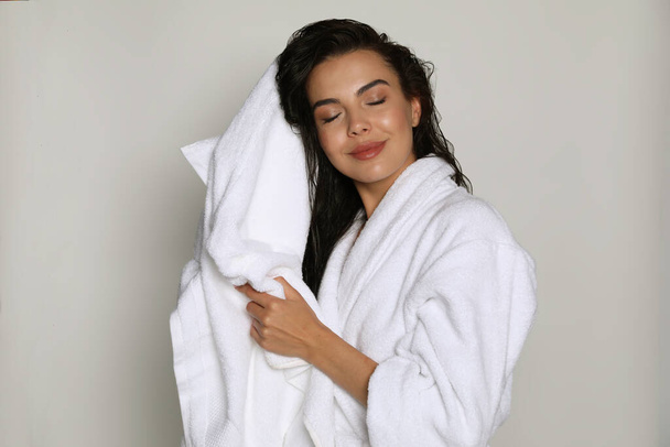 Beautiful young woman in bathrobe drying hair with towel on light background - Foto, Bild