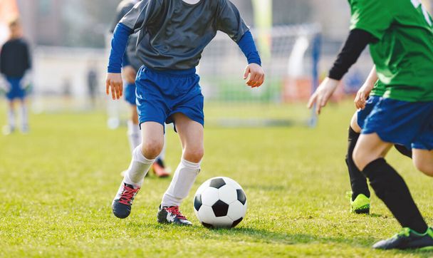 サッカートーナメントをプレイする小さな男の子はアウトに一致します。夏の晴れた日にサッカーゲーム。グレーとグリーンのジャージーの制服を着た学校の子供たち草のピッチ上で古典的なサッカーボールを実行 - 写真・画像