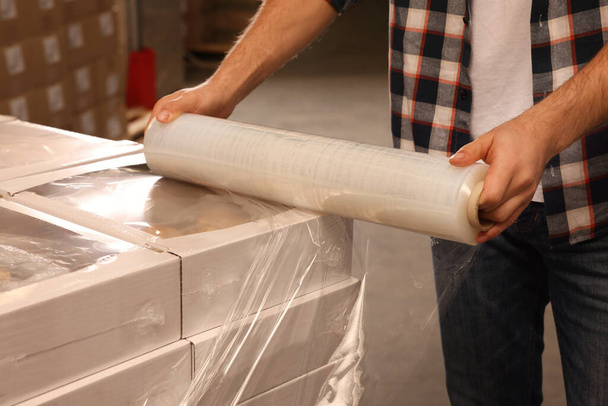 Worker wrapping boxes in stretch film at warehouse, closeup - Photo, Image