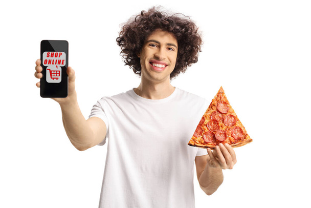 Cheerful young man holding a pizza slice and showing a smartphone with text shop online isolated on white background - Fotografie, Obrázek