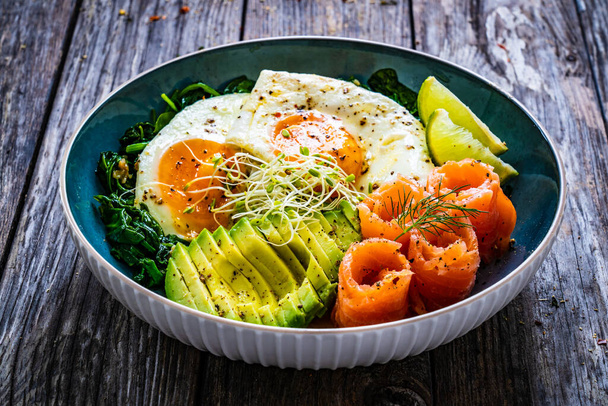 Salmon salad - smoked salmon, sunny side eggs, avocado and spinach on wooden table  - Photo, image