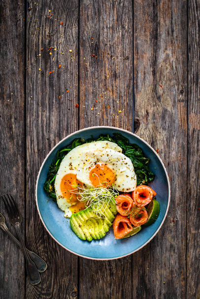 Salmon salad - smoked salmon, sunny side eggs, avocado and spinach on wooden table  - Photo, image