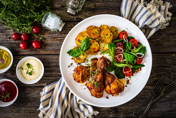 Barbecue chicken drumsticks with fried potato, lettuce and mini tomatoes on wooden table  - Zdjęcie, obraz