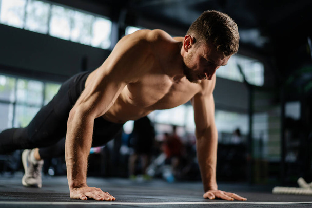 Man doing push ups in a gym. Exhaling and inhaling after push-ups and exercise. Perfect for fitness and workout. Young sports man performs pushups in the gym. The athlete is engaged in fitness - Photo, Image