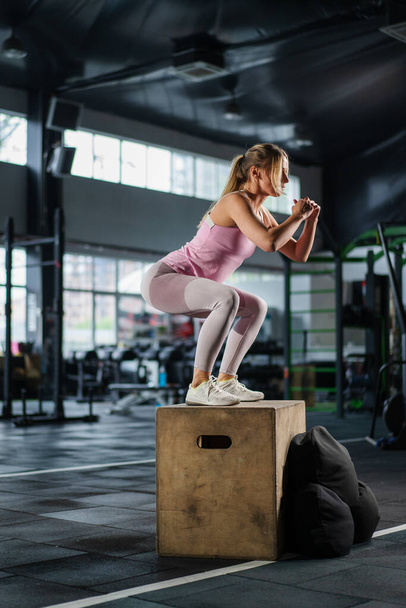 Sopii naisurheilija hyppää laatikko kehon koulutusta pimeässä kuntosalilla. Fitness nainen hypätä liikunta urheiluseurassa. Vahva tyttö sydän harjoitus. Fit kouluttaja laihtuminen käyttää rasvanpolttoa - Valokuva, kuva