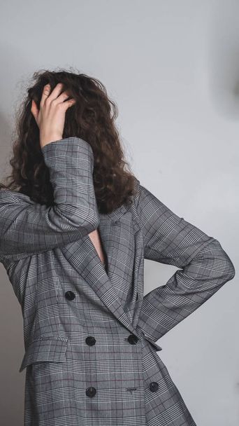 Un primo piano di una ragazza in abiti alla moda in posa contro un muro grigio - Foto, immagini