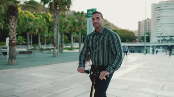 Giovane uomo d'affari vestito in camicia guardando fiducioso cavalcando scooter elettrico sulla riunione di lavoro. Bellissimo ragazzo guida calci scooter attraverso la città - Filmati, video