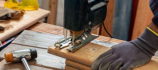 Sierra eléctrica, carpintero guante de mano cortando madera con un rompecabezas eléctrico. Industria de la construcción, mesa de trabajo vista de primer plano - Foto, Imagen
