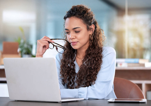 Schnappschuss einer attraktiven jungen Geschäftsfrau, die nachdenklich wirkt, während sie im Büro an ihrem Laptop arbeitet. - Foto, Bild