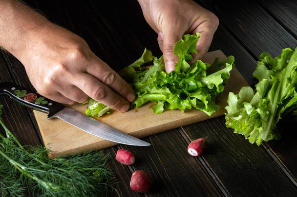 The cook prepares a salad on a kitchen cutting board. Close-up of chef's hands on the table while preparing food. - Foto, Imagem