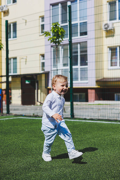 A little boy 2 years old in a shirt and trousers runs and laughs. A child on a sunny day rejoices and smiles. - Foto, Imagen
