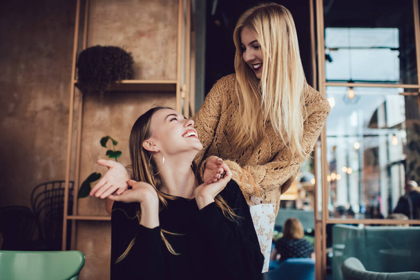 Cheerful ladies with long hairs in casual clothes laughing and looking at each other during meeting in contemporary outdoor terrace - Fotografie, Obrázek