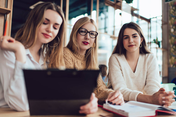 Focused female freelancers in casual clothing sitting at wooden table with clipboard and working on project together in modern cafe - Foto, Bild