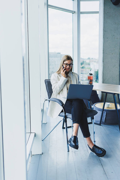 Mosolygó üzletasszony laptopot néz, miközben az irodában dolgozik. A modern sikeres nő koncepciója. Az ötlet az üzleti és az élet egy vállalkozó. Fiatal nő asztalnál nyitott laptoppal - Fotó, kép
