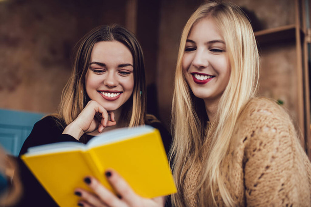 Charming cheerful friends in casual clothing enthusiastically reading notes in copybook and laughing while having rest in cozy room - Фото, изображение