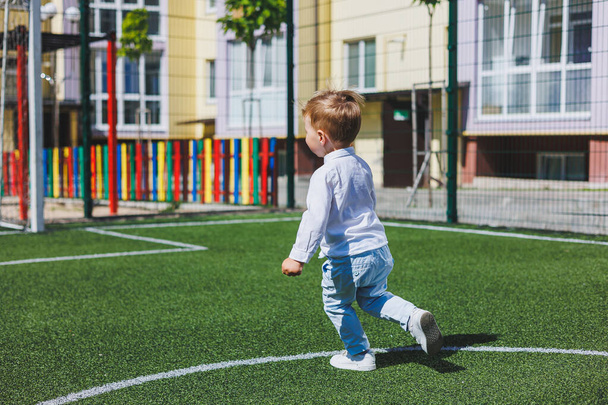 Ein kleiner Junge von 2 Jahren in Hemd und Hose rennt und lacht. Ein Kind an einem sonnigen Tag freut sich und lächelt. - Foto, Bild