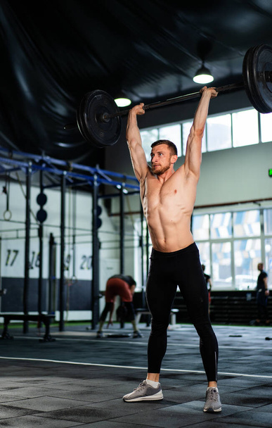 Athletic man doing overhead barbell press in hardcore gym - Photo, image