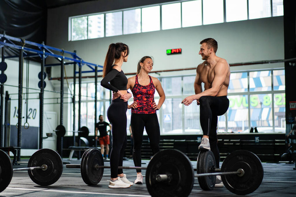 Athletic sport male athlete communicates with fit girls after training in hardcore gym. Fitness healthy man and woman tired after strength training exercise at gym. - Foto, Imagen