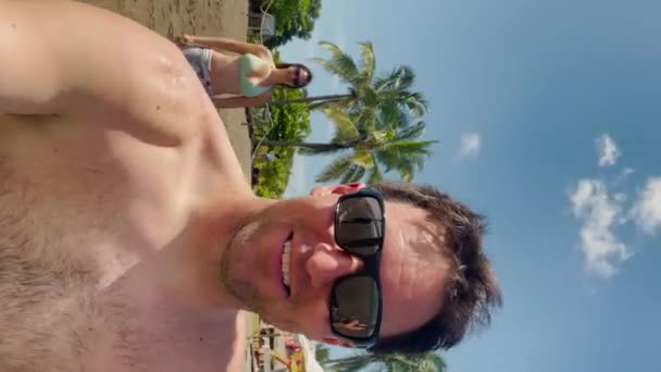 Glimlachende jongeman op het strand geduwd door een jonge vrouw. Speels en vrolijk zomermoment op vakantie op exotische locatie. Vrijetijdsbesteding in Playa Venao in Panama. - Video