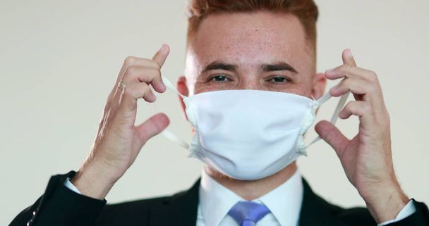 Knappe roodharige zakenman die chirurgische maskers verwijdert na een pandemie. persoon verwijderd covid-19 masker - Foto, afbeelding
