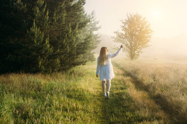 Frau weiß gekleidet am Sommermorgen spazieren gehen und den schönen Wald bei Sonnenaufgang genießen - Foto, Bild