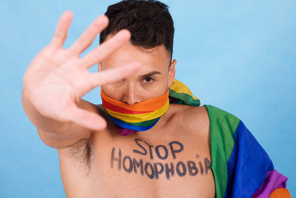 Tvůrčí portrét gaye s protestními vzkazy na hrudi, s roubíkem plným pýchy a vztyčenou rukou na protest. Kvalitní fotografie - Fotografie, Obrázek