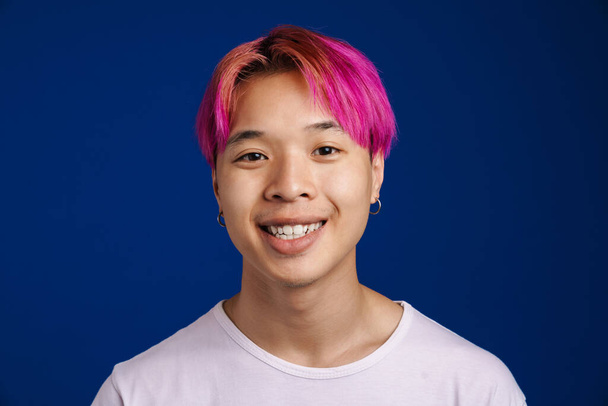 Asian boy with pink hair smiling and looking at camera isolated over blue background - 写真・画像