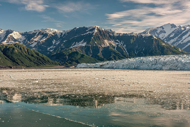 Kiábrándító öböl, Alaszka, USA - 2011. július 21.: Lebegő jégmező a Hubbard gleccser jégfal előtt az óceán szintjén. Hóval borított hegyvonulat a láthatáron a kék felhő alatt. Erdős lejtők - Fotó, kép