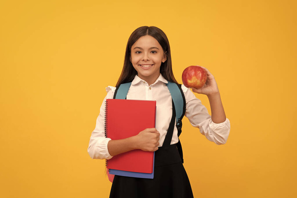 Ευτυχισμένο παιδί πάει πίσω στο σχολείο κρατώντας μήλο και βιβλία κίτρινο φόντο, ημέρα της γνώσης. - Φωτογραφία, εικόνα