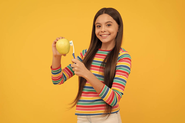 Happy girl dziecko szczoteczka jabłko ze szczoteczką do zębów żółte tło, higiena jamy ustnej. - Zdjęcie, obraz