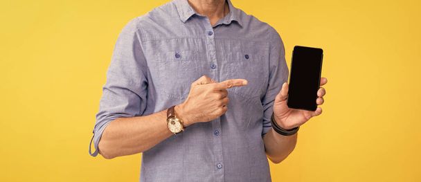 hombre recortado señalando el dedo en el teléfono inteligente sobre fondo amarillo, espacio para copiar, presentando el producto. - Foto, imagen