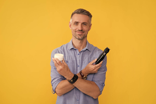 man hold electric razor and cream on yellow background, skin. - Foto, afbeelding