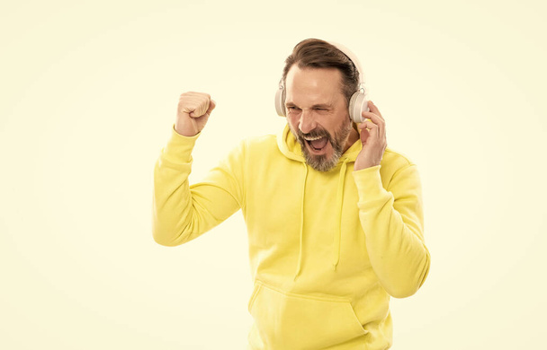 homem maduro alegre com barba e bigode com capuz ouvir música ou livro de áudio em fones de ouvido isolados em branco, música. - Foto, Imagem