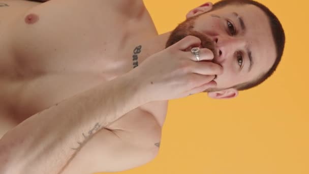 Tatuoitu paidaton mies koskettaa hänen viiksensä ja hymyilee pystysuora video keltainen tausta studio ammuttu. Laadukas 4k kuvamateriaalia - Materiaali, video