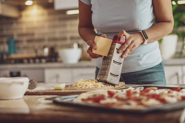 Le mani delle donne strofinano il formaggio per la pizza pronta per la cottura sullo sfondo della cucina - Foto, immagini